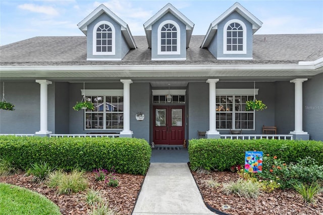 view of exterior entry with covered porch and a shingled roof