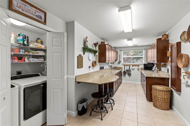 kitchen featuring a textured ceiling, a sink, light tile patterned floors, washing machine and clothes dryer, and baseboards
