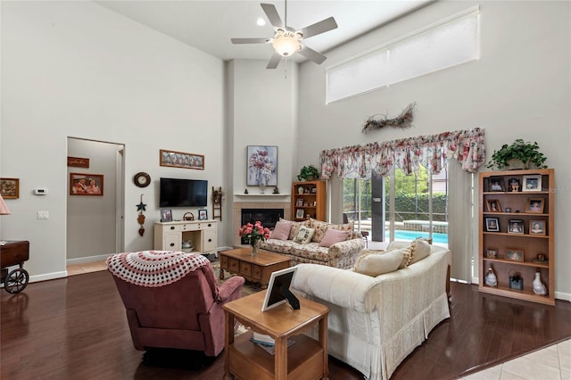 living area with a high ceiling, ceiling fan, wood finished floors, baseboards, and a tile fireplace