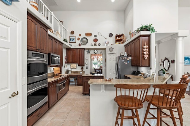 kitchen with stainless steel appliances, a high ceiling, a peninsula, light tile patterned floors, and a kitchen breakfast bar