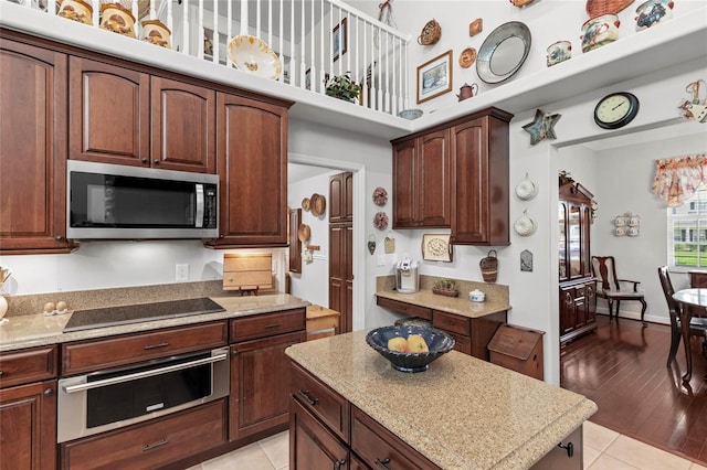 kitchen featuring appliances with stainless steel finishes, a towering ceiling, a warming drawer, light tile patterned floors, and a kitchen island