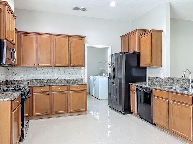 3731 Peaceful Valley Dr, Clermont, FL 34711 - kitchen featuring black appliances, washing machine and dryer, dark stone countertops, and brown cabinets