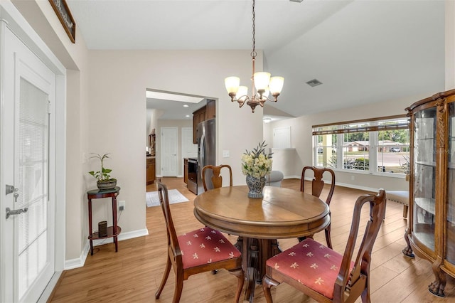 dining space featuring light wood-style floors, a chandelier, vaulted ceiling, and baseboards