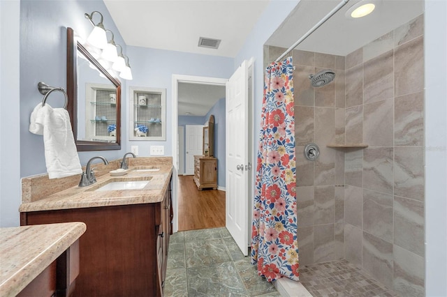 full bath featuring tiled shower and double vanity