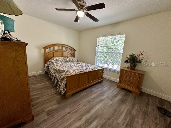 bedroom with dark wood-style floors, baseboards, a ceiling fan, and a textured ceiling