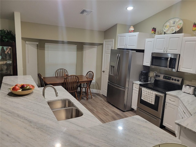 kitchen featuring appliances with stainless steel finishes, a sink, light wood-style flooring, white cabinetry, and light stone counters