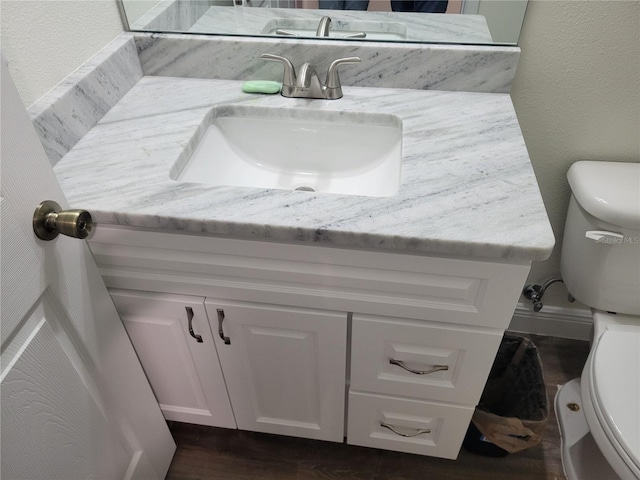 half bath with toilet, vanity, wood finished floors, and a textured wall