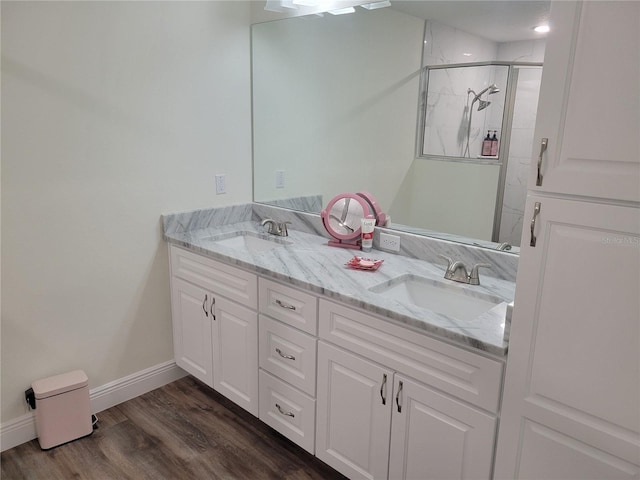 bathroom featuring a shower stall, wood finished floors, double vanity, and baseboards