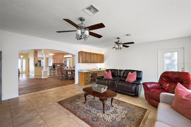 2096 Callaway Dr, The Villages, FL 32162 - living room with arched walkways, ceiling fan, light tile patterned floors, ornate columns, and a textured ceiling
