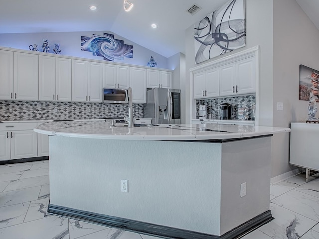 kitchen with stainless steel appliances, light marble finish floors, lofted ceiling, a center island with sink, and white cabinetry