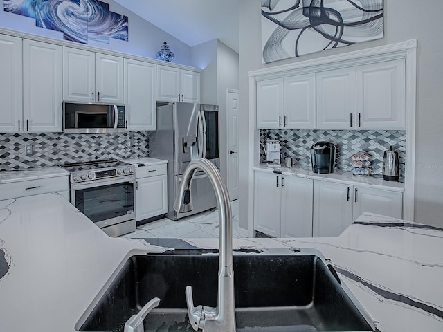 kitchen with appliances with stainless steel finishes, a sink, tasteful backsplash, white cabinetry, and lofted ceiling