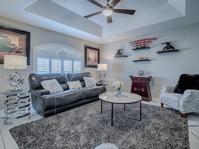 living area featuring a ceiling fan, a tray ceiling, baseboards, and marble finish flooring