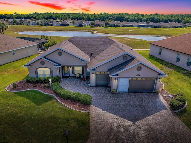 ranch-style house with a water view, a garage, decorative driveway, and a front yard