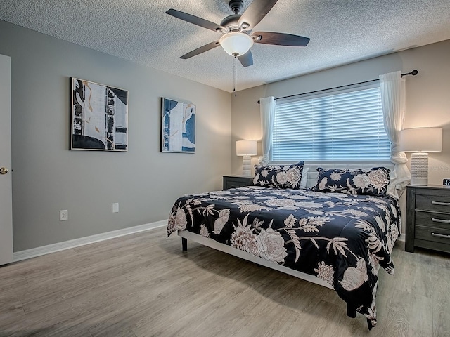 bedroom with light wood-style flooring, a textured ceiling, baseboards, and ceiling fan