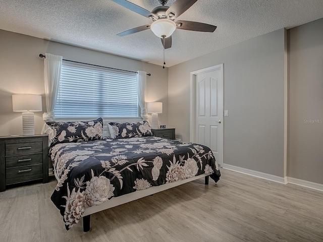 bedroom with light wood finished floors, a textured ceiling, baseboards, and a ceiling fan