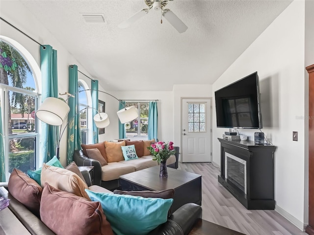 1202 Del Toro Dr, Lady Lake, FL 32159 - living area featuring a textured ceiling, ceiling fan, a glass covered fireplace, light wood-type flooring, and vaulted ceiling