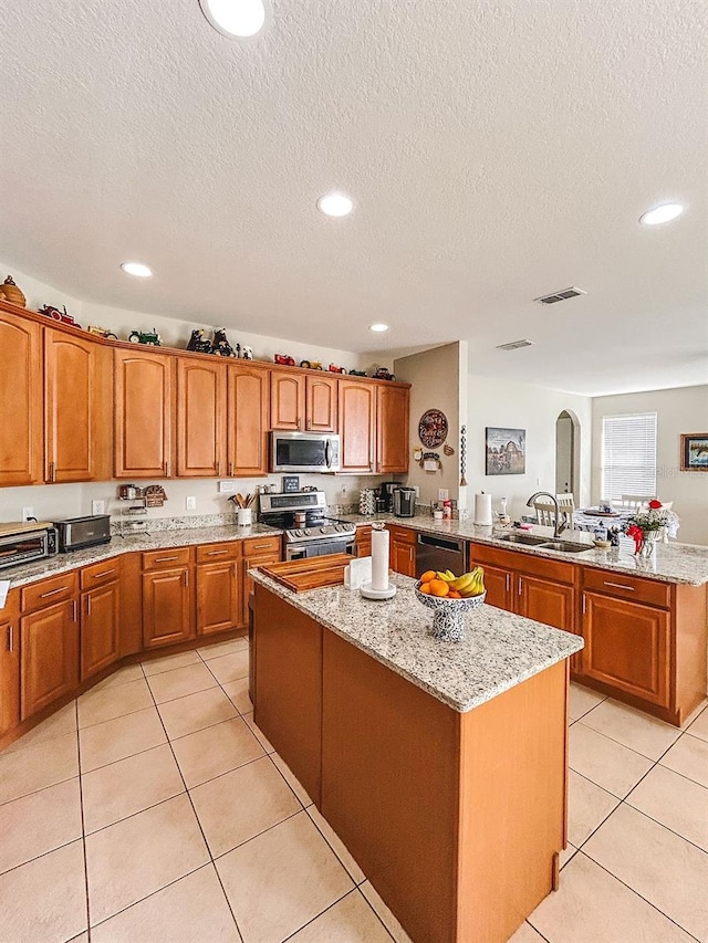 33818 Venice Ln, Sorrento, FL 32776 - kitchen featuring stainless steel appliances, a sink, a kitchen island, brown cabinetry, and a peninsula