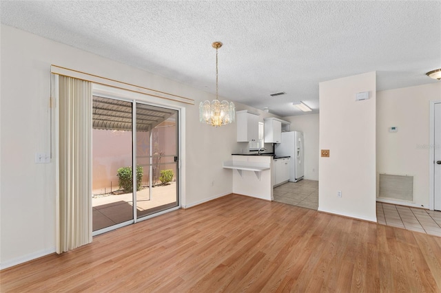 403 Duarte Ln, The Villages, FL 32159 - unfurnished living room with light wood-style floors, a chandelier, a textured ceiling, a sink, and baseboards