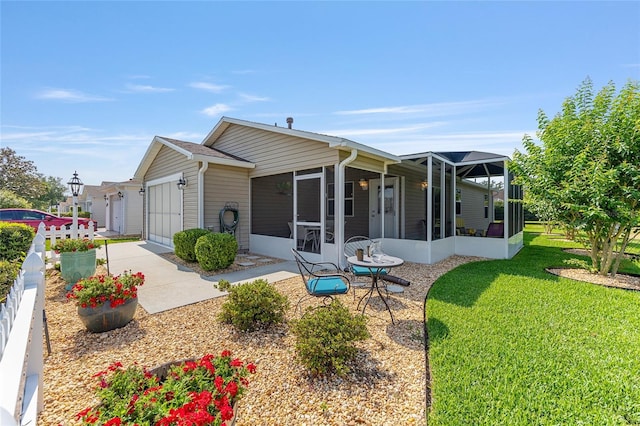 back of house with a sunroom, an attached garage, a yard, and driveway