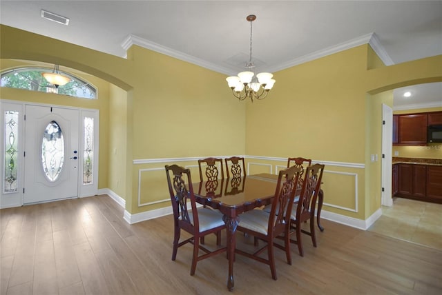 1828 Hollow Branch Way, The Villages, FL 32162 - dining room featuring a chandelier, light wood finished floors, ornamental molding, wainscoting, and arched walkways