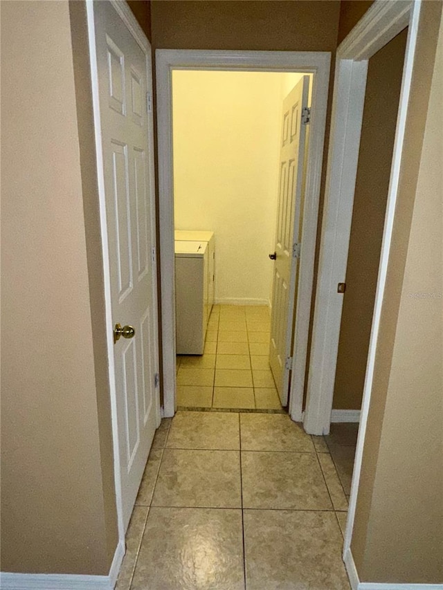corridor with washing machine and clothes dryer, light tile patterned floors, and baseboards
