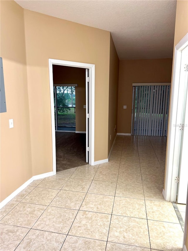hall featuring light tile patterned flooring, baseboards, a textured ceiling, and electric panel