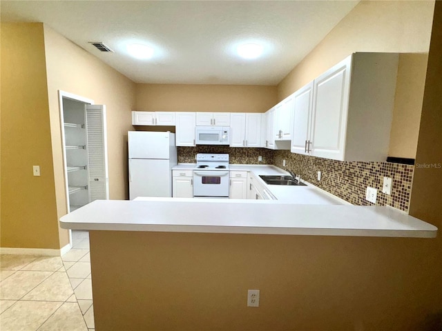 kitchen featuring white appliances, a peninsula, a sink, white cabinets, and tasteful backsplash