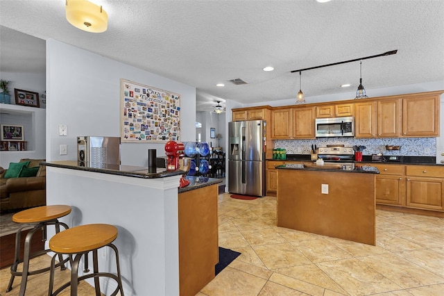 kitchen featuring appliances with stainless steel finishes, a center island, dark countertops, a kitchen breakfast bar, and backsplash