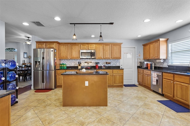 kitchen featuring appliances with stainless steel finishes, a sink, a kitchen island, backsplash, and dark countertops