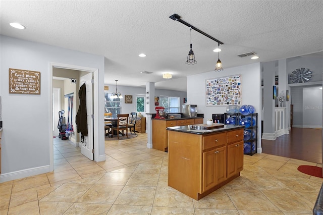 kitchen featuring a textured ceiling, dark countertops, a center island, brown cabinets, and pendant lighting