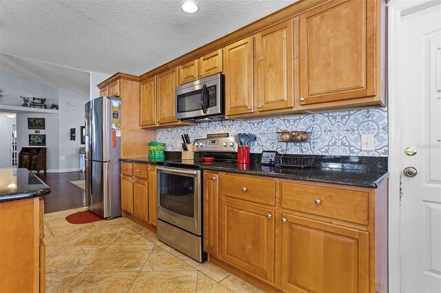 kitchen with stainless steel appliances, brown cabinetry, decorative backsplash, dark stone countertops, and a textured ceiling