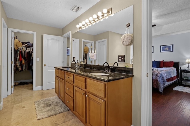 bathroom with a textured ceiling, connected bathroom, double vanity, baseboards, and a spacious closet