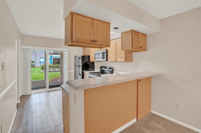 kitchen with appliances with stainless steel finishes, a peninsula, light brown cabinets, light countertops, and baseboards