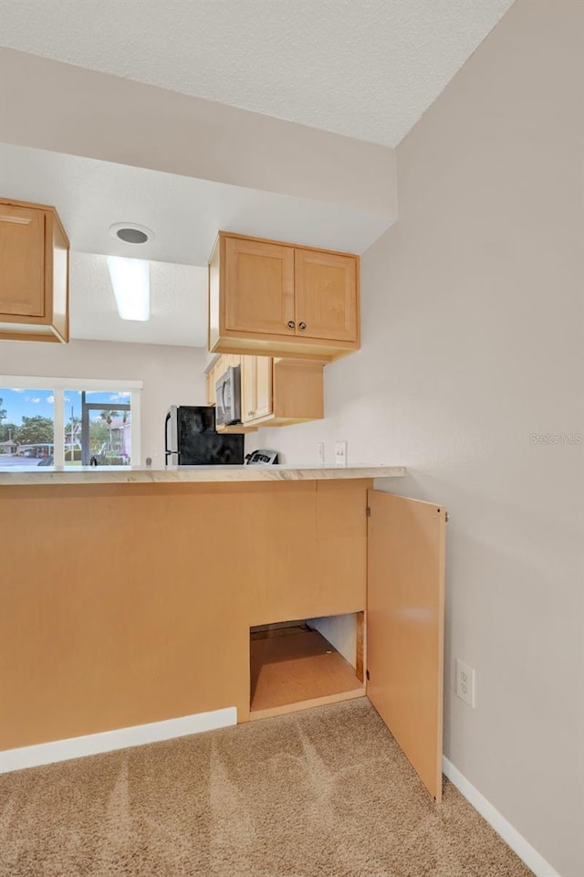 kitchen featuring carpet floors, baseboards, stainless steel microwave, freestanding refrigerator, and light brown cabinets