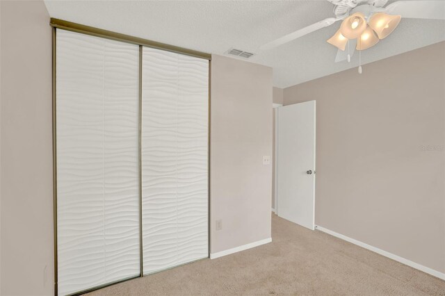 unfurnished bedroom featuring light colored carpet, a closet, a ceiling fan, baseboards, and a textured ceiling