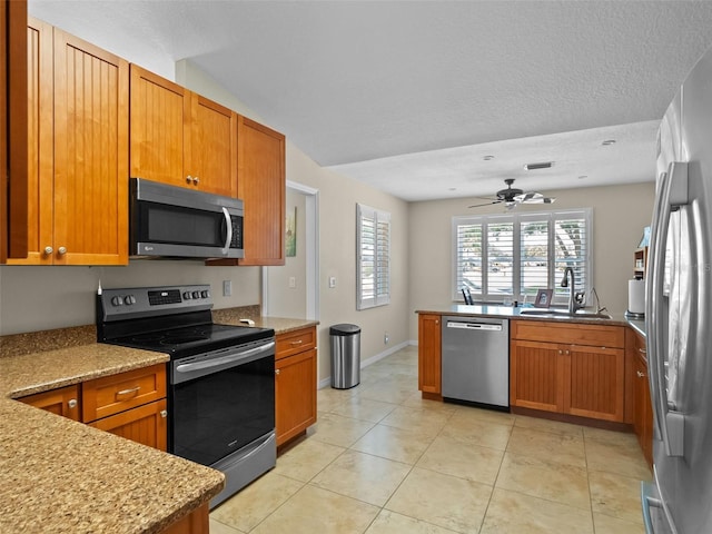 kitchen featuring stainless steel appliances, a sink, ceiling fan, brown cabinetry, and a textured ceiling