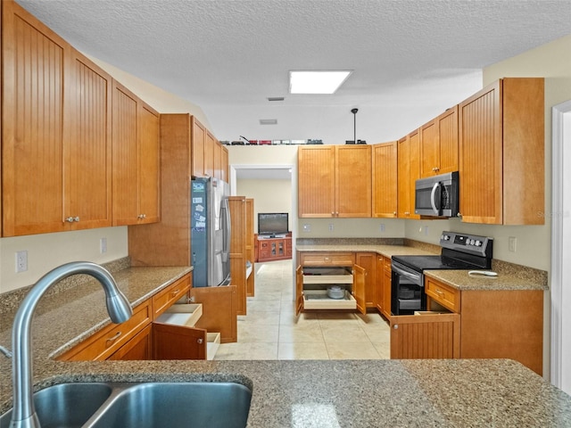 kitchen featuring appliances with stainless steel finishes, a sink, a textured ceiling, stone countertops, and light tile patterned flooring