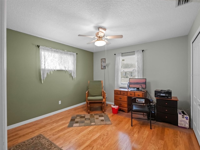 home office featuring light wood-style flooring, a ceiling fan, a textured ceiling, and baseboards