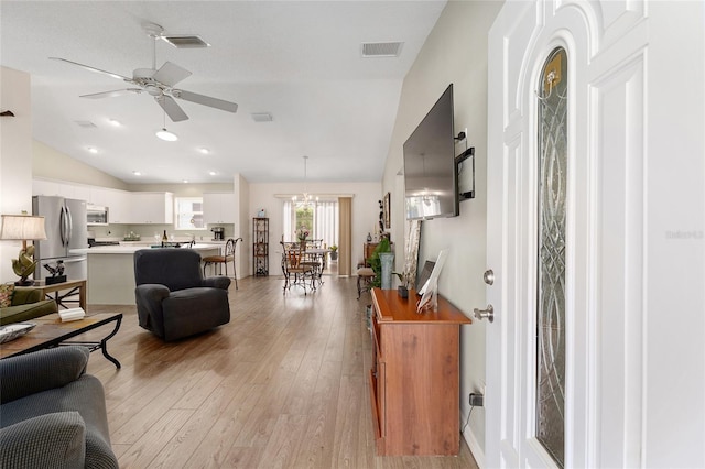 living room featuring vaulted ceiling, light wood-type flooring, ceiling fan, and a chandelier