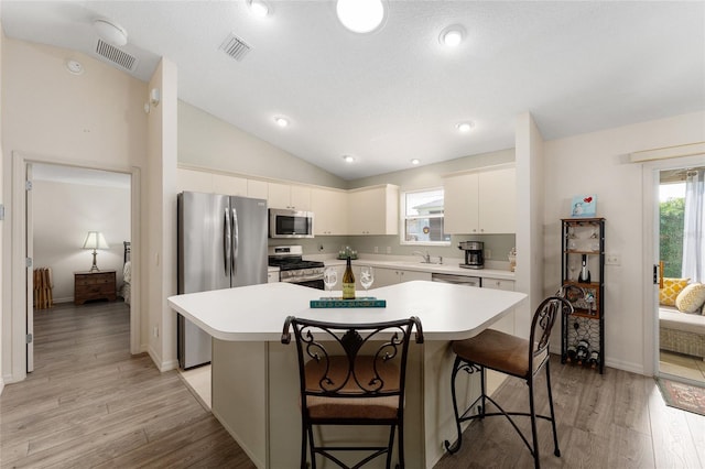 kitchen with appliances with stainless steel finishes, a kitchen island, light countertops, a breakfast bar, and lofted ceiling