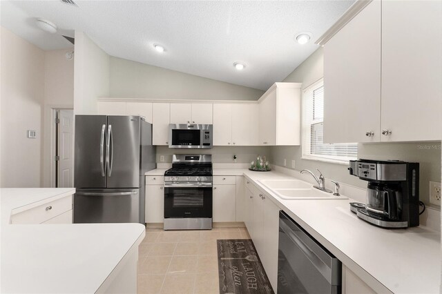 kitchen with stainless steel appliances, a sink, light countertops, lofted ceiling, and white cabinetry