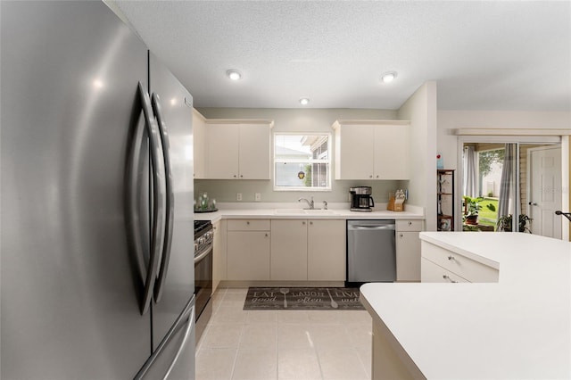 kitchen with stainless steel appliances, a sink, light countertops, light tile patterned floors, and a textured ceiling