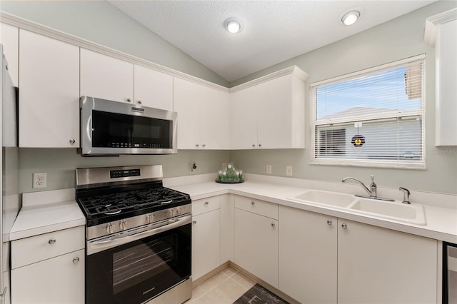 kitchen with appliances with stainless steel finishes, vaulted ceiling, a sink, light countertops, and light tile patterned floors