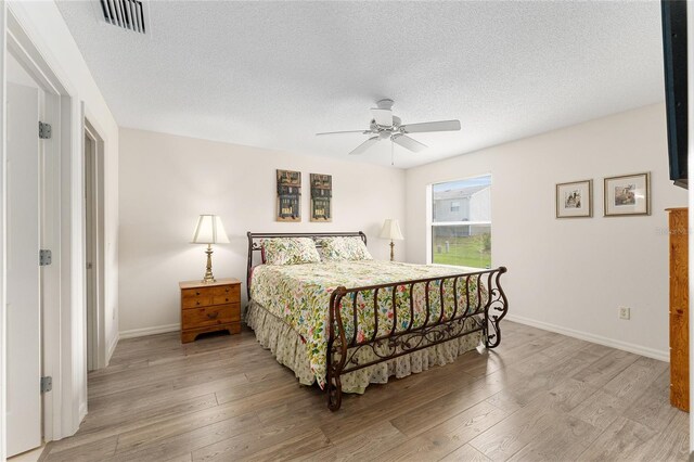 bedroom with a textured ceiling, light wood-type flooring, baseboards, and ceiling fan