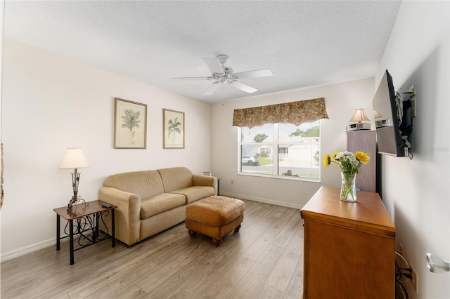 living area with light wood-style flooring, a ceiling fan, baseboards, and a textured ceiling