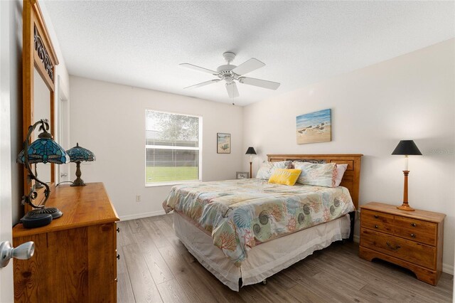 bedroom with wood finished floors, baseboards, ceiling fan, and a textured ceiling