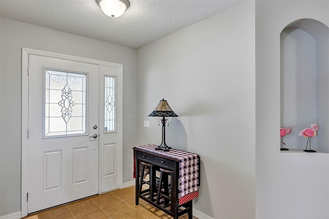 entrance foyer with a textured ceiling, light tile patterned floors, arched walkways, and baseboards