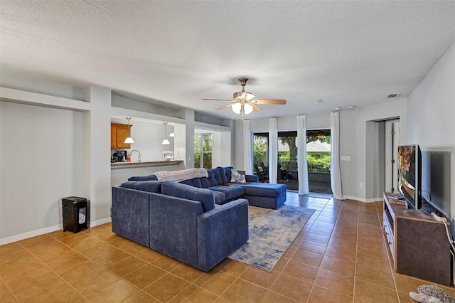 living area featuring plenty of natural light, tile patterned floors, ceiling fan, and a textured ceiling