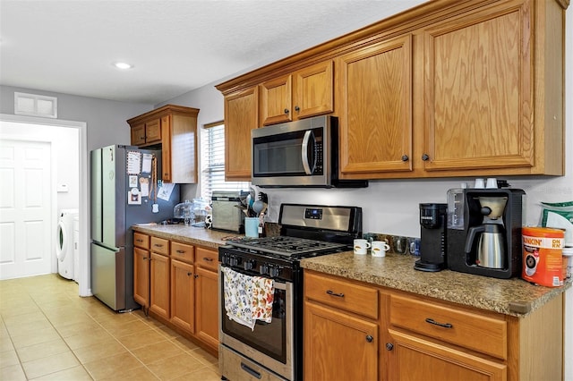 kitchen featuring stainless steel appliances, washer / clothes dryer, brown cabinetry, light tile patterned flooring, and recessed lighting