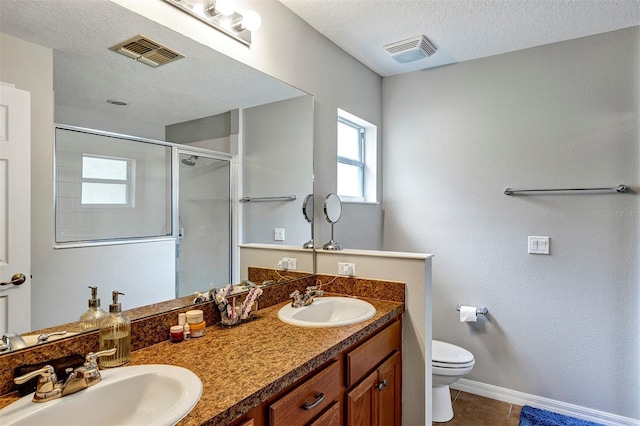 full bathroom with a stall shower, toilet, a textured ceiling, baseboards, and double vanity